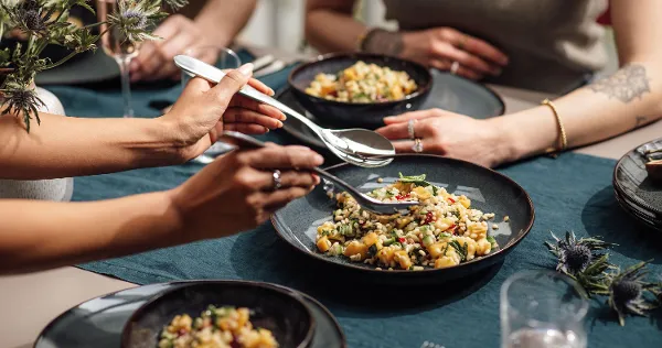 Lave bowls with mixed salad are placed on a blue tablecloth. Four people enjoy a meal at one table. Lave bowls with mixed salad are placed on a blue tablecloth.