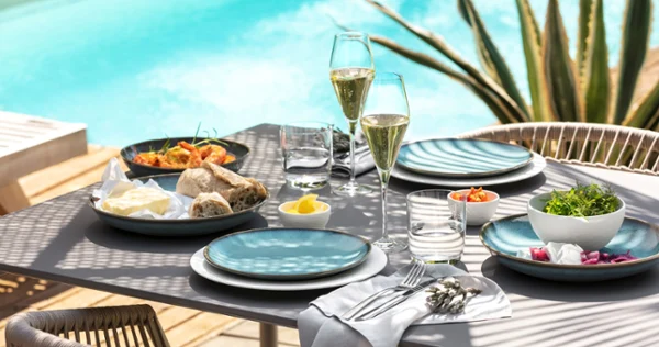 Al Fresco Poolside Table Setting A beautifully set outdoor dining table with plates, glasses of champagne, bread, and fresh salads beside a swimming pool.