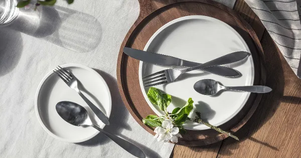 Elegant table decoration with simple white plates and Arthur Brushed stainless steel cutlery, accentuated by natural light and a sprig of flowers.