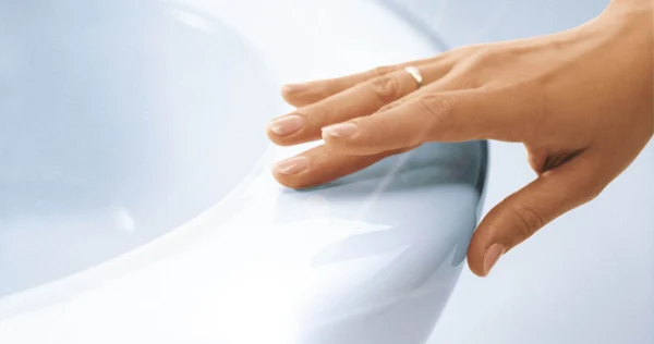 Close-up of a hand with a gold ring touching the rim of a shiny white ceramic toilet.