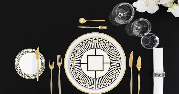 Elegant dining table decoration with gold-patterned MetroChic plates, gold cutlery and crystal glasses viewed from above.