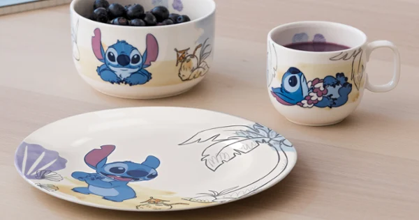 A plate, a bowl of blueberries and a mug with Stitch and Lilo designs on a wooden table.