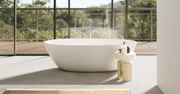 A white Antao bath in a room with a glass wall and trees.