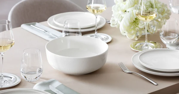 Large, empty Afina serving bowl from Villeroy & Boch on a set table with flowers in the background.