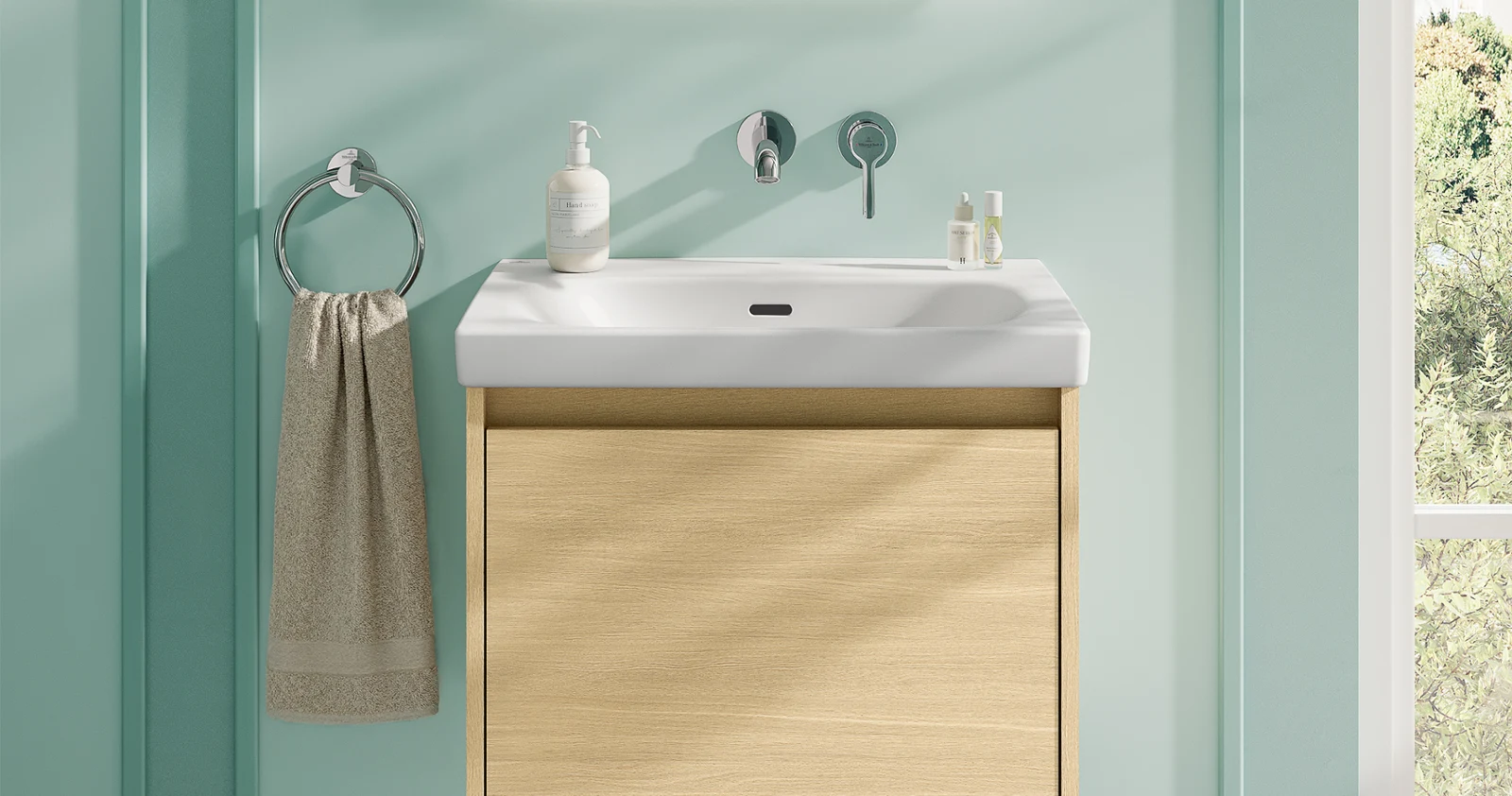 Serviette beige sur un meuble-lavabo dans une salle de bains verte Salle de bains moderne avec un meuble-lavabo en bois clair, un lavabo blanc, un miroir mural et une serviette suspendue à un anneau métallique devant un mur vert menthe.