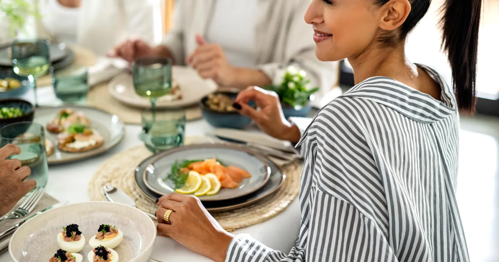 Et bord dekket med beige Lave-servise fra like. by Villeroy & Boch med mennesker som spiser sammen.