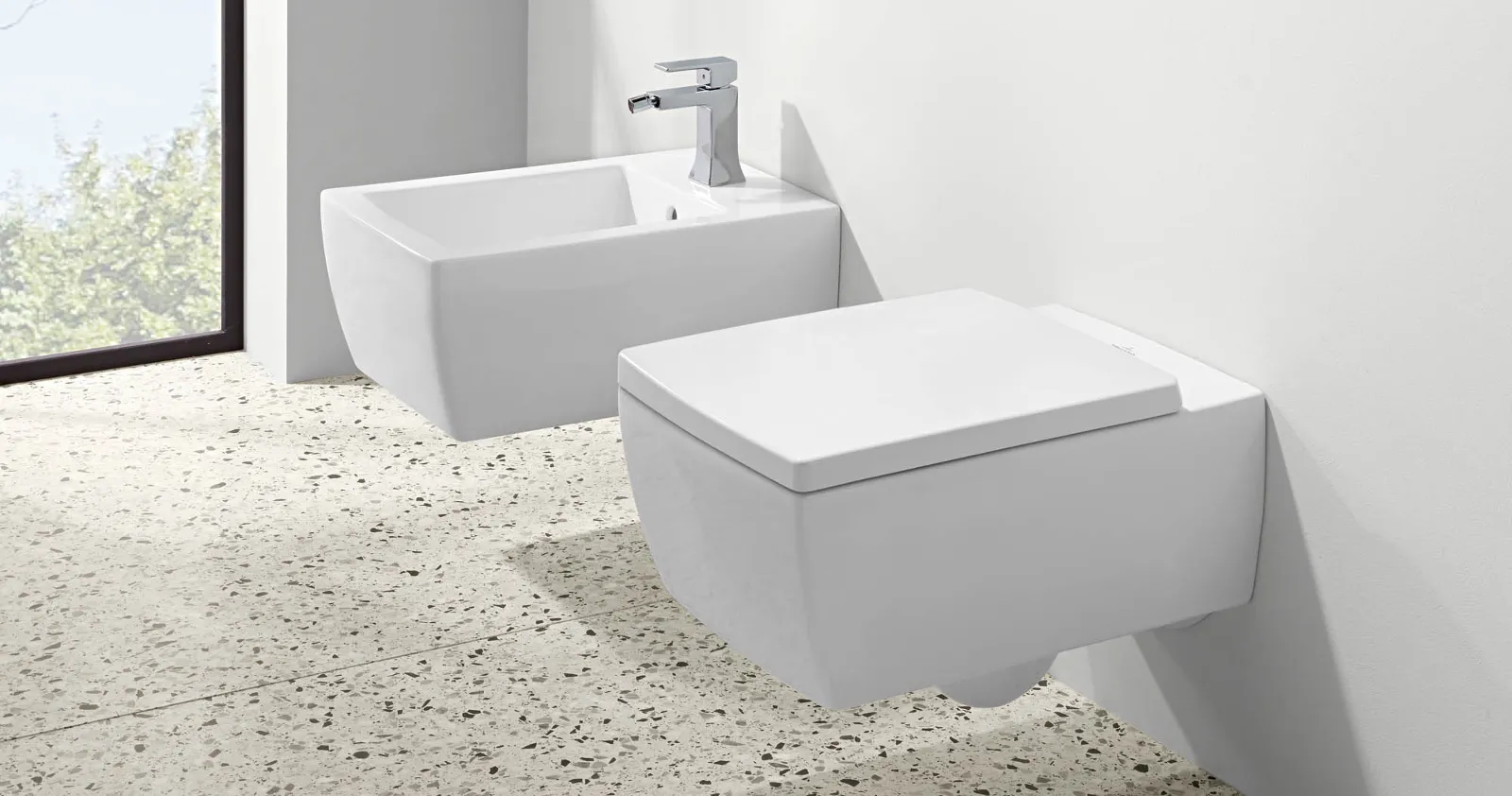 Arredo bagno moderno e minimalista con bidet e WC bianchi davanti a un'ampia finestra
