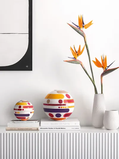 La Boule Miami dekorativ in Szene gesetzt Ein minimalistisches Sideboard zeigt die moderne La Boule Miame, Vasen, Paradiesvogelblumen und gestapelte Bücher unter abstrakter Wandkunst.