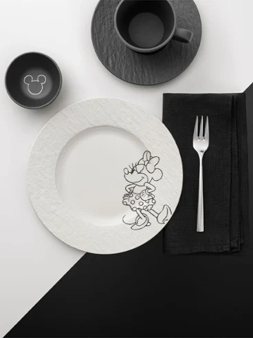 A black and white table setting from the Manufacture Mickey collection with a plate, fork, cup and bowl on a colour-divided background.
