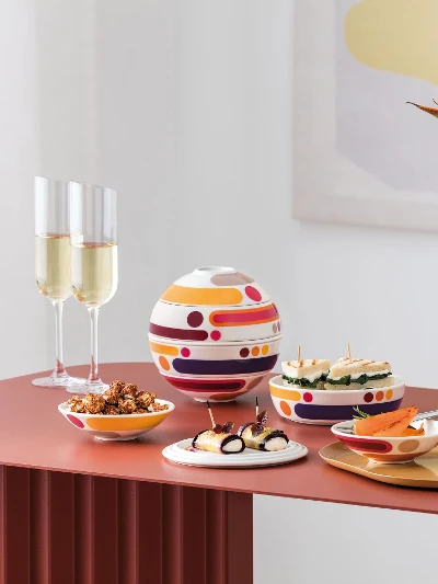 La Boule Miami with Manufacture Blanc Collier Vase in modern arrangement A modern table setting with La Boule Miami, assorted snacks, two champagne glasses, and a white Manufacture vase Collier with orange flowers.