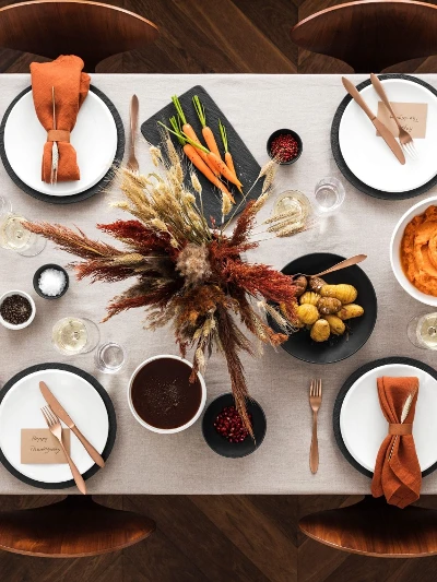 A table set with dishes, roast turkey, vegetables, mashed potatoes, greens, bread, and an autumnal floral arrangement in the center.