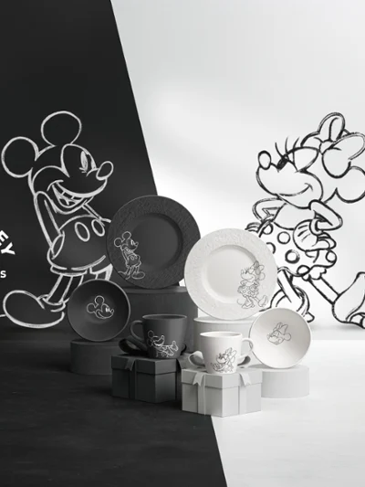 A range of black and white plates and cups from the Manufacture Mickey collection has been expanded. A set of black and white plates and cups from the Manufacture Mickey collection, arranged on a surface divided into black and white halves.