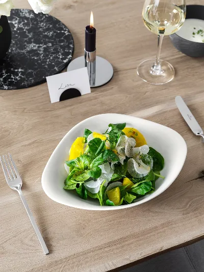 A Villeroy & Boch Vapiano bowl with salad on a wooden table, beside a NewWave knife and fork.