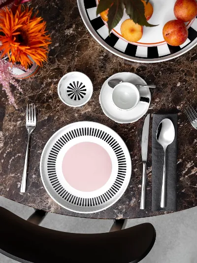Farbexplosion mit Memphis von Villeroy & Boch Ein runder Marmortisch mit zwei Memphis Gedecken, jeweils mit einem Teller, Besteck und einer Tasse. Eine Schale mit Äpfeln und eine Memphis Vase mit Blumen schmücken die Mitte.