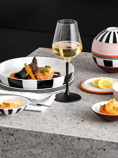 Frutti di mare guarniti su La Boule Memphis di Villeroy & Boch Una tavola imbandita in modo moderno con un bicchiere di vino bianco, frutti di mare serviti, pane affettato e spicchi di limone su un piano di lavoro in granito.