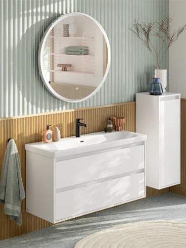 Bagno moderno con uno specchio rotondo, un mobile lavabo bianco, un pensile, un asciugamano e un vaso decorativo davanti a una parete strutturata.