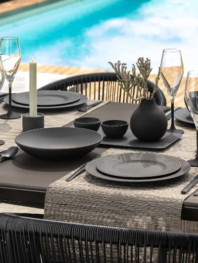 Elegant outdoor dining area with black crockery and glasses from the Manufacture collection beside a pool.