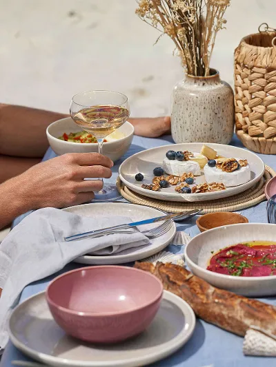 A couple sitting at a table on the beach with plates from the like. by Villeroy & Boch Perlemor collection.