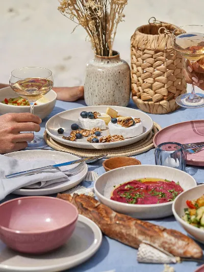 A couple sitting at a table on the beach with plates from the like. by Villeroy & Boch Perlemor collection.