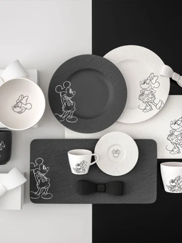 L'intera collezione Manufacture Mickey con piatti, tazze e ciotole bianchi e neri su uno sfondo diviso in bianco e nero.
