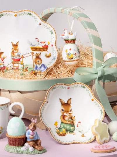 A decorative Annual Easter Edition 2026 basket A decorative Annual Easter Edition 2026 basket with bunny-themed plates, cup, figurine, cookies, eggs, and a green ribbon.
