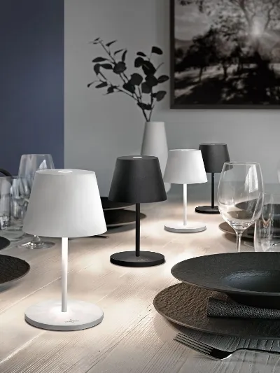 Ein Esstisch mit schwarzen und weißen Seoul Leuchten Ein moderner Esstisch mit schwarzen Manufacture Tellern, Gläsern und kleinen Tischlampen, im Hintergrund Kunstwerke und eine Vase.
