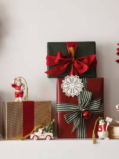 Festive Christmas shelf with wrapped presents, Christmas decorations from Villeroy & Boch, a wreath with red and silver ornaments from Villeroy & Boch, and a vase with red flowers and green plants.