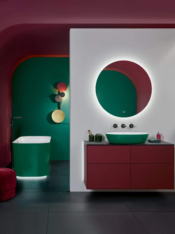 Zielona umywalka Artis w łazience w intensywnych kolorach Nowoczesne wyposażenie łazienki w mocnych kolorach z wanną wolnostojącą Finion, ciemnozieloną umywalką Artis i okrągłym, podświetlanym lustrem More to See