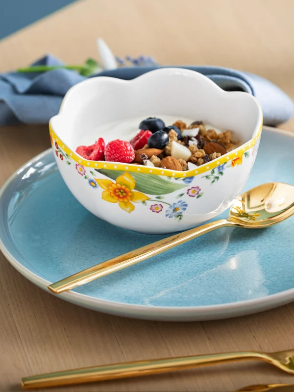 A breakfast set consisting of a Spring Awakening cereal bowl and a light-blue Crafted plate, with a gold spoon and a cup of tea on the side.