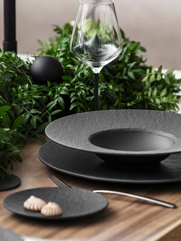 Create una tavola elegante con la collezione Manufacture di Villeroy & Boch, caratterizzata da eleganti piatti neri, un bicchiere da vino e un rigoglioso centrotavola verde. Create una calda atmosfera a lume di candela ponendo due candele nere non accese accanto a un'unica candela rosa accesa. Completate la scena con piccoli dessert, presentati con eleganza su un piatto da contorno.