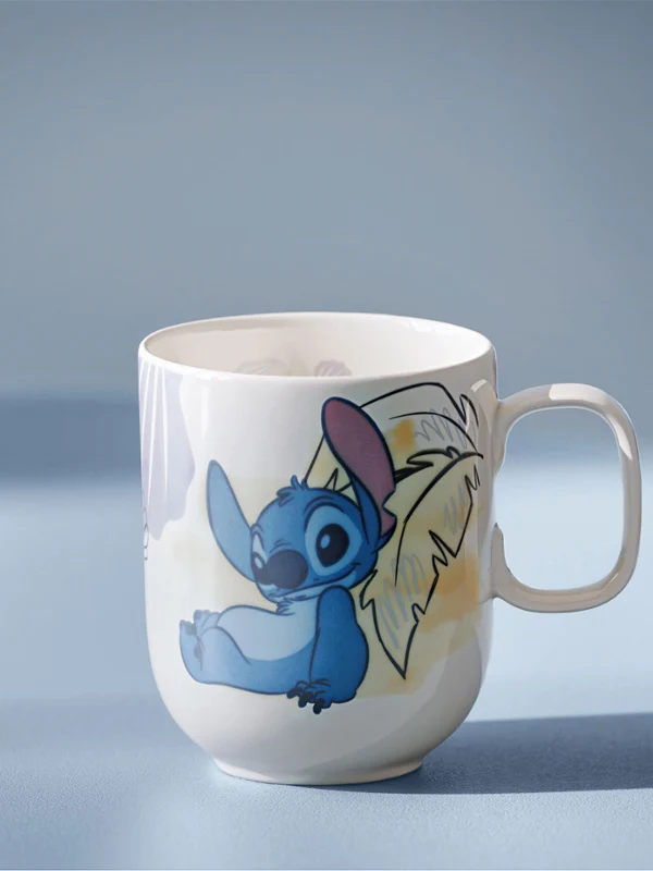 Taza blanca de Disney Stitch sobre una superficie azul claro. Taza blanca con una ilustración de Stitch, de la película Lilo & Stitch de Disney, sobre un fondo azul claro.