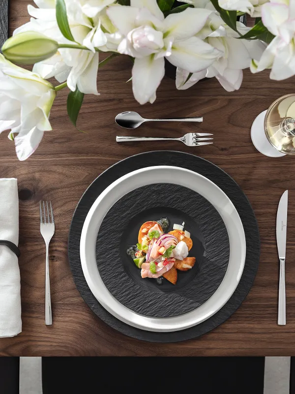 Décoration de table élégante avec un plat de fruits de mer sur des assiettes Manufacture, des fleurs blanches, un verre de vin blanc et une petite assiette avec des tranches de citron.