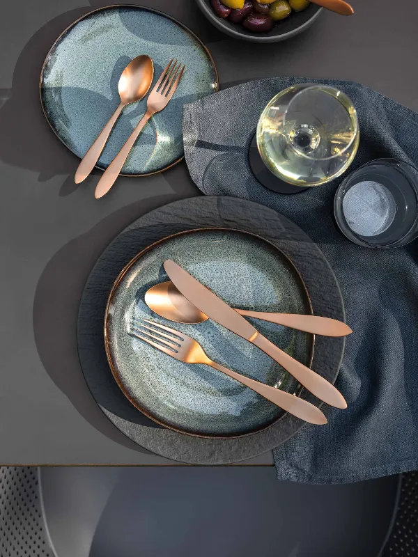 Elegant table decoration with two Lave plates, Manufacture cutlery, a bowl of olives and a glass of white wine on a grey tablecloth.