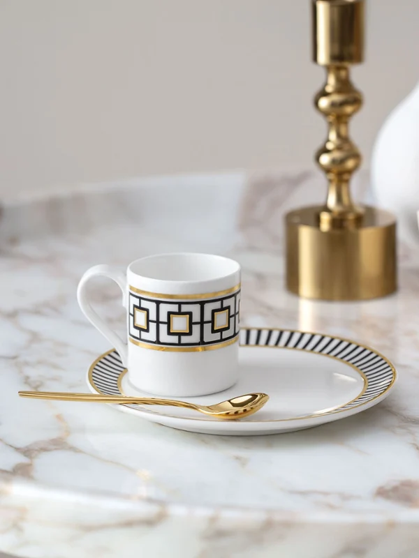 Eine goldene MetroChic Kaffeetasse mit Untertasse auf einem Marmortisch.