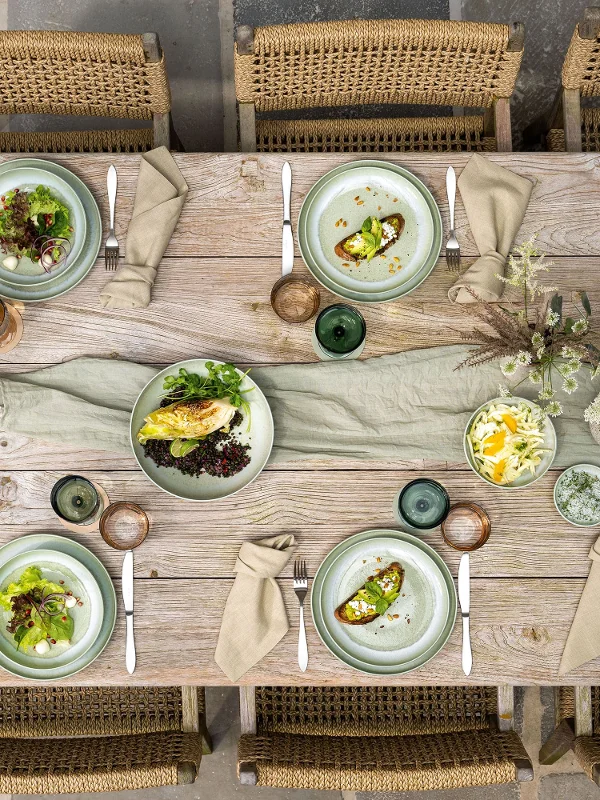 Vue de dessus d'une table à manger rustique pour six personnes avec des assiettes Perlemor, des boissons et des fleurs décoratives.