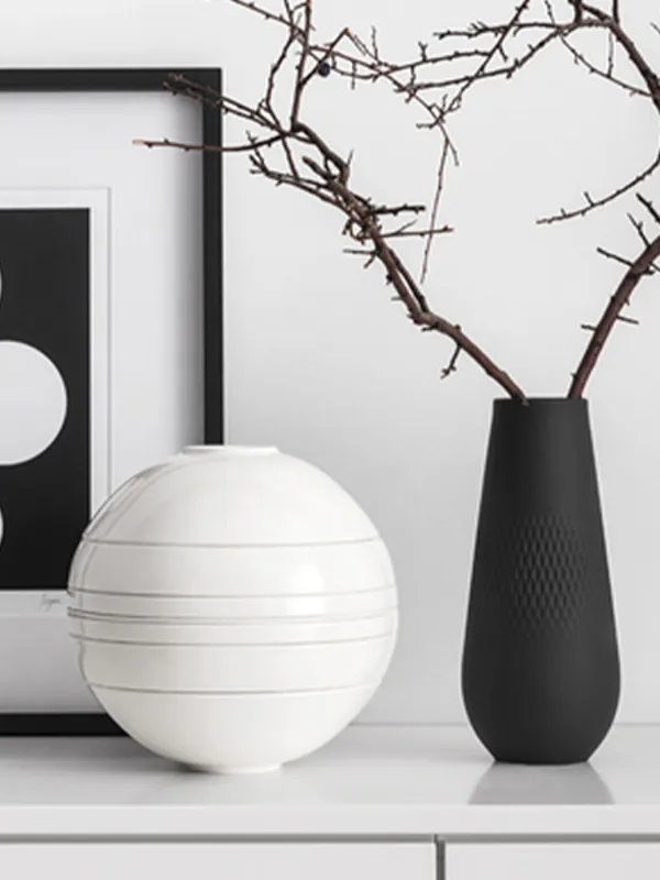 Arte astratta incorniciata, un vaso rotondo bianco e un vaso nero con rami su una superficie bianca.