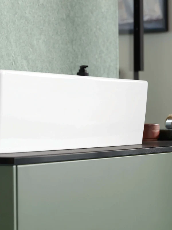 Detail view of the Memento 2.0 washbasin in glossy white with black tap – fine contours and minimalist elegance on a green vanity unit.