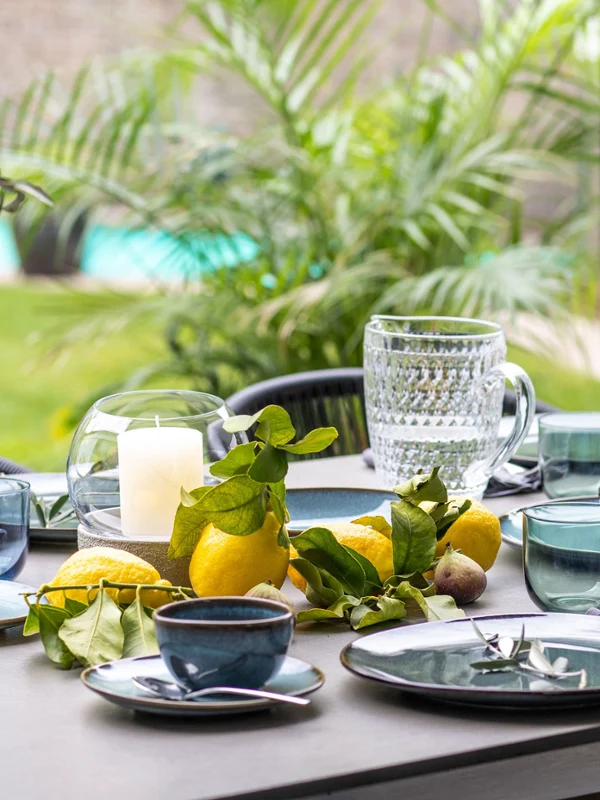 Esstisch im Freien mit Lave Geschirr, Gläsern, Kerzen und frischen Zitrusfrüchten als Tafelaufsatz mit Blick auf einen Pool.