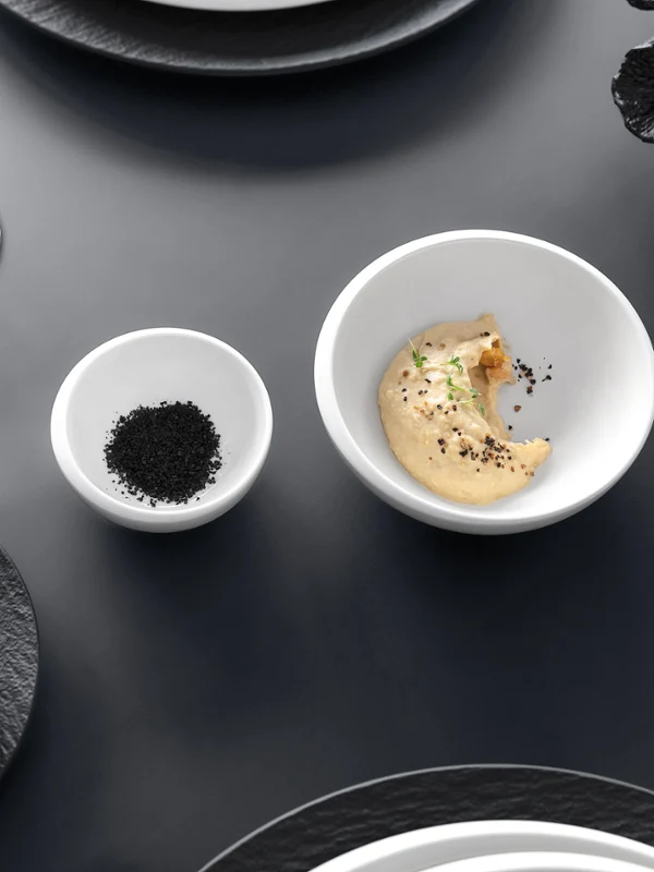 Topshot eines eleganten Esszimmers mit einer NewMoon Schale, einer kleinen Schale mit Gewürzen und gefüllten Weingläsern auf einem grauen Tisch.