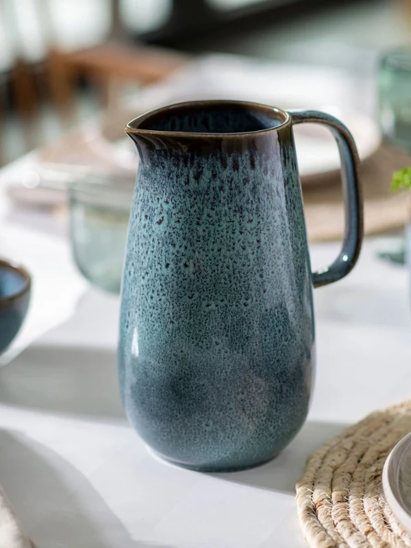 Ein Lave-Krug und dazu passende Schüsseln auf einem Esstisch, elegant gedeckt und von natürlichem Licht erhellt.