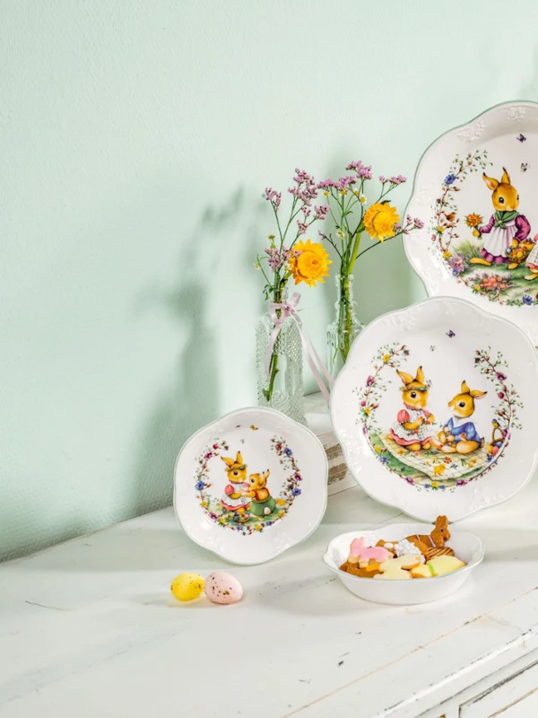 Four easter bowls decorated with bunnies, an easter mug and a some flower pots with spring flowers in them all sitting on a white wood dining sideboard