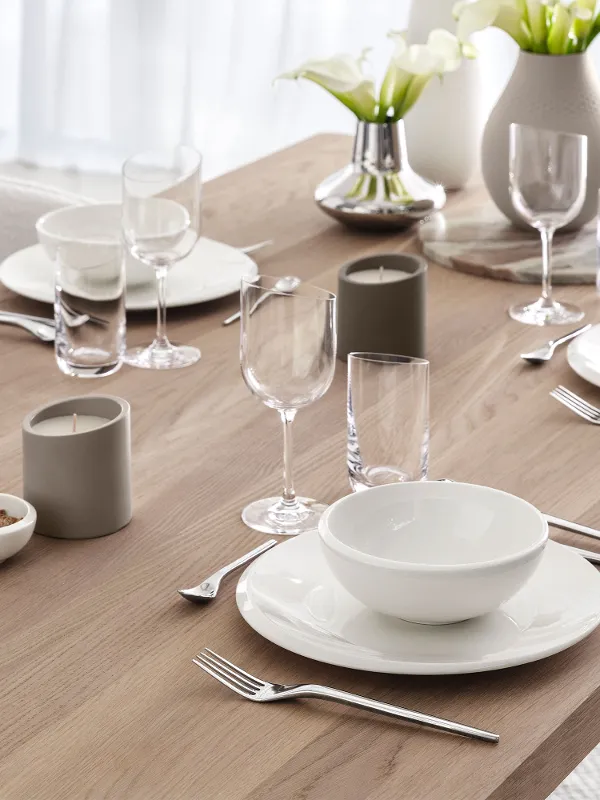 Une table en bois à la décoration minimaliste avec des assiettes NewMoon, des verres et des bougies parfumées