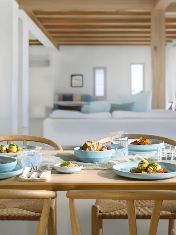 Ein hölzerner Esstisch für vier Personen mit blauen Perlemor Aqua Tellern in einem hellen, modernen Wohnbereich.
