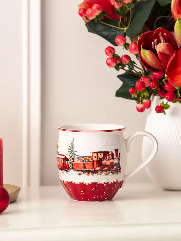 Red candles, a festive mug, red ornaments, and a vase with red flowers on a white surface.