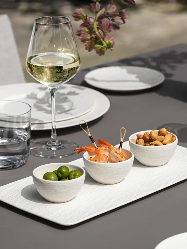 Elegant outdoor table setting with white Manufacture crockery, starters and white wine.