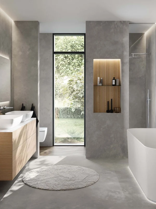 Baño minimalista con bañera "Finion" de Villeroy & Boch, mueble bajo lavabo "Finion" y dos lavabos "Artis". El sencillo diseño combina elementos de madera natural con modernas paredes grises y un gran ventanal para crear un ambiente luminoso y sosegado.