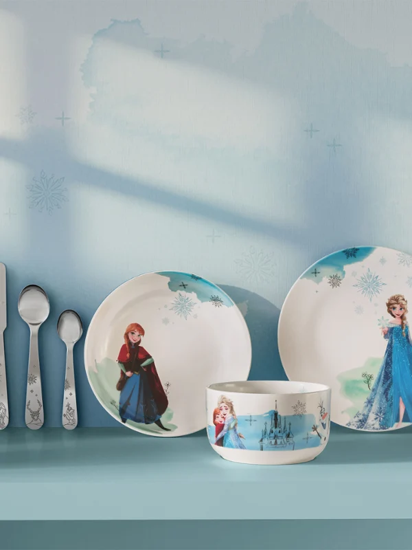 Vajilla y utensilios infantiles con personajes de Frozen, expuestos en una estantería azul. Vajilla y utensilios infantiles con personajes de Frozen, expuestos con cajas de regalo azules en una estantería azul.