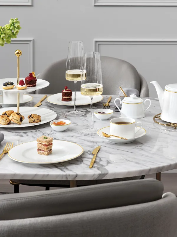 A marble table set for afternoon tea with desserts, pastries, tea service, champagne glasses and a flower arrangement.