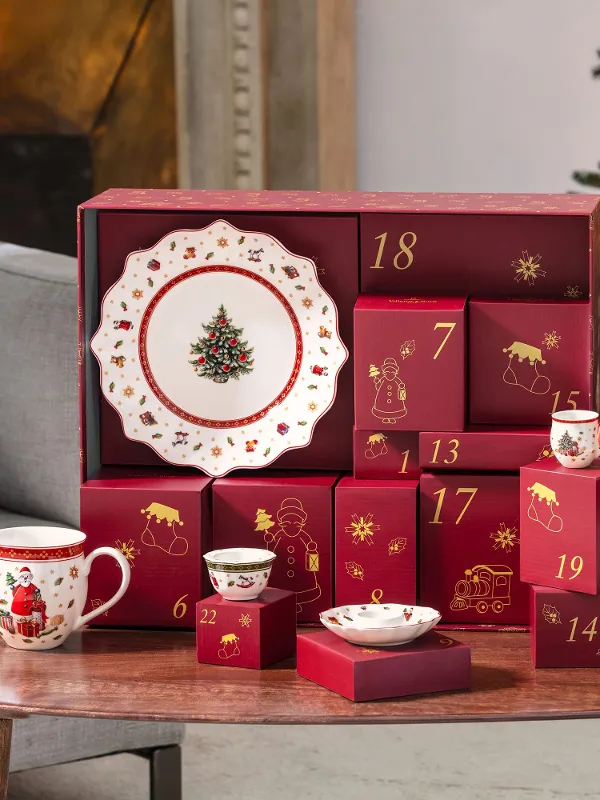 Scatole rosse del calendario dell'Avvento e stoviglie natalizie sono poste su un tavolo di legno accanto a un albero di Natale decorato.