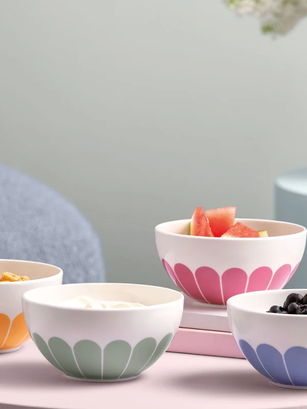 Villeroy & Boch Fleur bowls with various foods placed on pastel-coloured tables next to books and a vase with flowers.